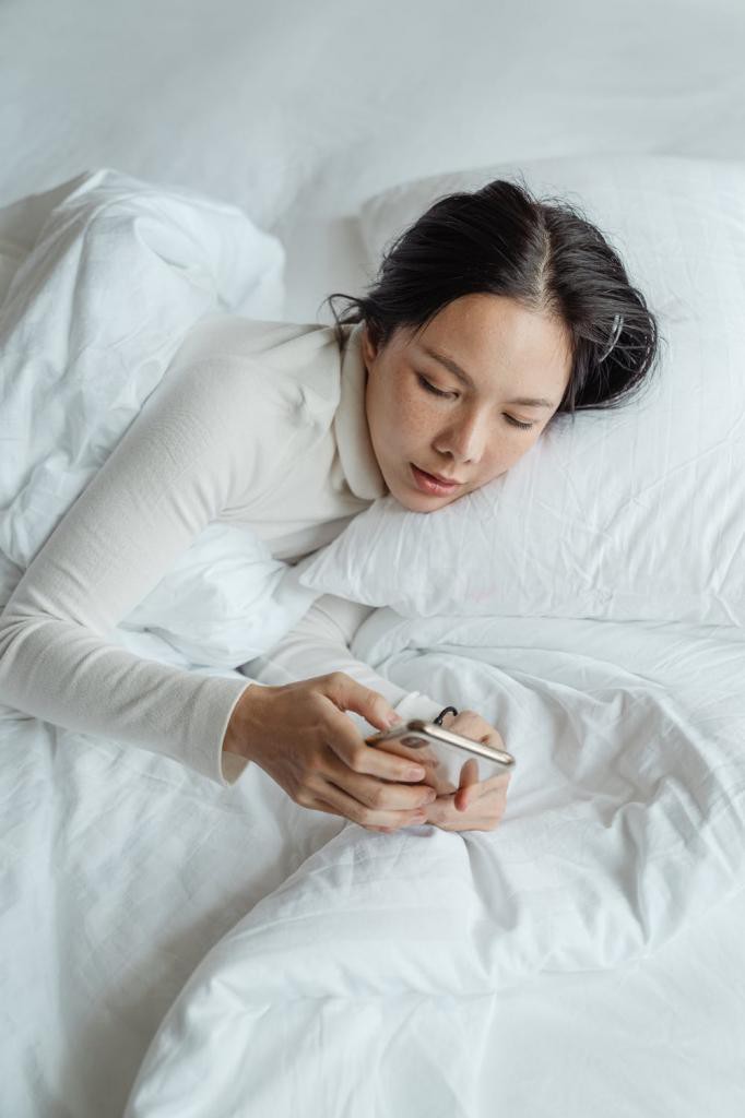 Positive woman waking up and using smartphone in bed