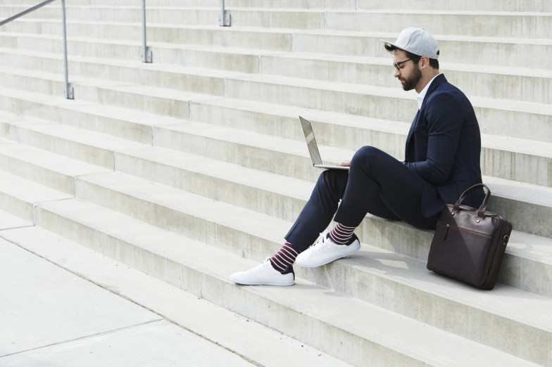 Man in suit and hat sitting on stairs using laptop