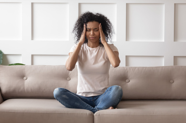 Upset stressed young african woman massage temples feel strong headache concept, frustrated tired black girl touching aching head suffer from migraine high blood pressure sitting on sofa at home