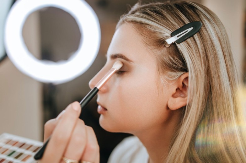 Close up shot of beautiful young woman face getting make-up. The artist is applying eyeshadow base with brush. Professional beautician work.
