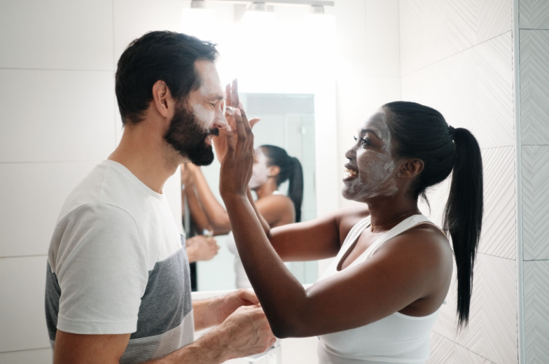 Woman Applying Beauty Mask And Skin Cleanser To Man