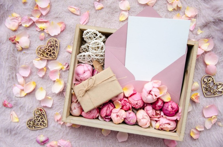 Valentine's Day composition. Gift box with handmade gift box, craft blank card, envelope, rose buds and decorative hearts on pink background with rose petals.Copy space. Template postcard for holiday