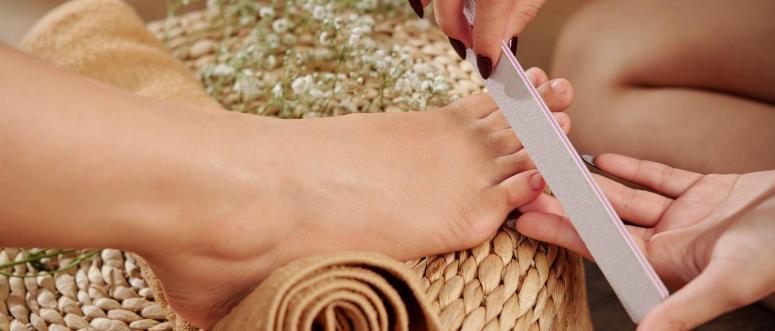 Close-up image of pedicurist filing nails of female client