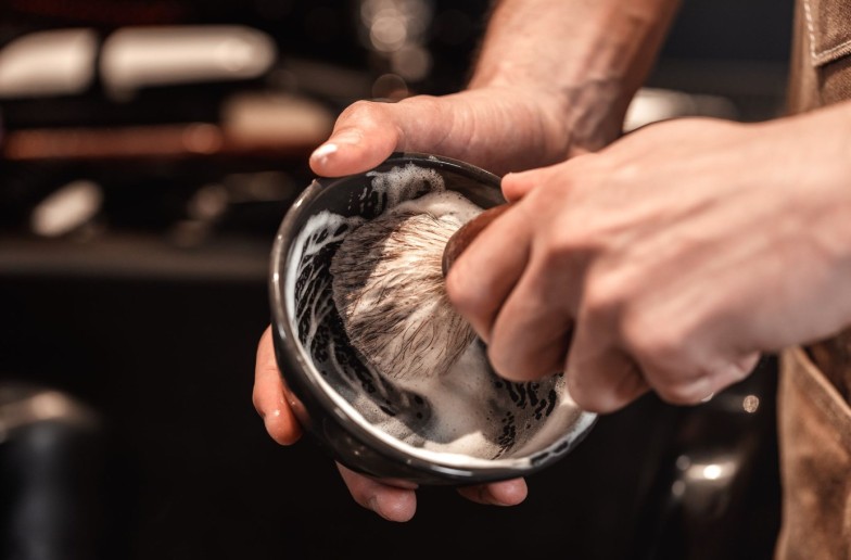 hands of barber with brush for shaving beard and bowl. barber shop
