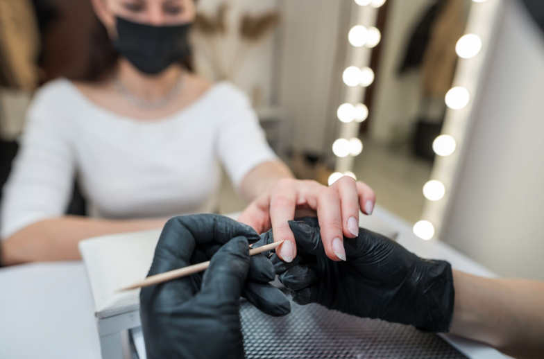 Nail salon. Professional beautician cleaning client's nails with orange stick, cuticle pusher, cuticle removal in beauty salon. Woman hands, nail care and manicure