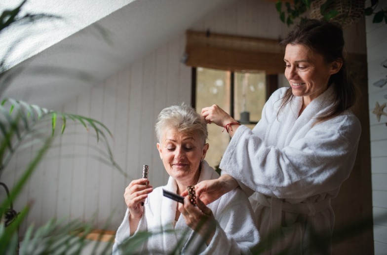 Happy senior mother in bathrobe with adult daughter indoors at home, selfcare concept.