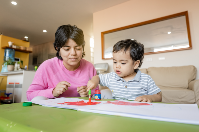 Latin mother and little son painting together with tempera colors.
