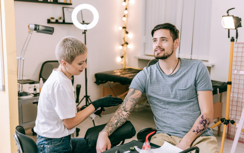 Tattoo sleeve Smiling appealing tattoo artist checking process of recovery of last tattoos of her male client