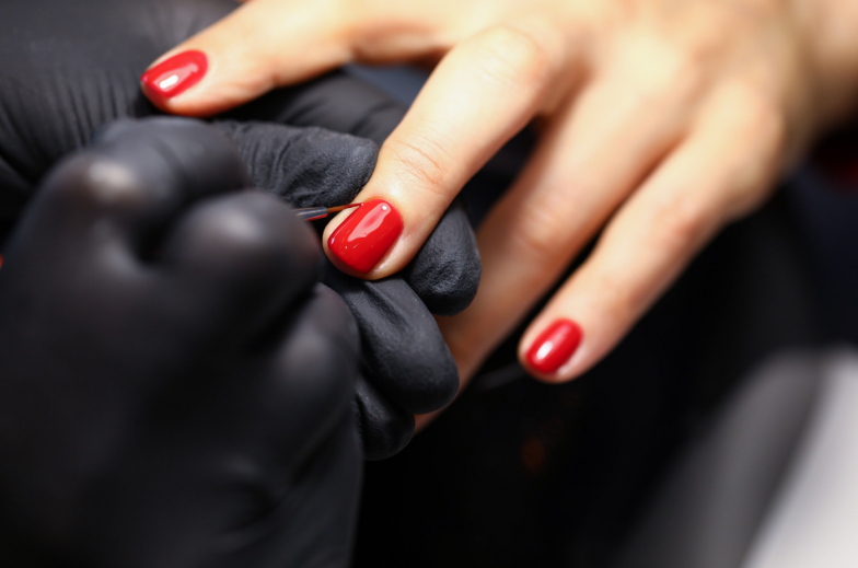 Close-up of manicure master painting clients nails in red colour
