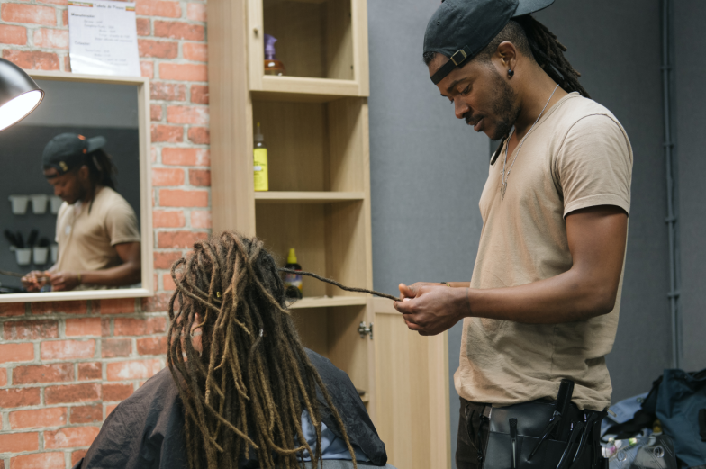 African master hairdresser making dreadlocks for young woman in hair salon
