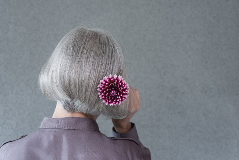 Silver-haired lady with red dahlia flower, on gray background with copy space.
