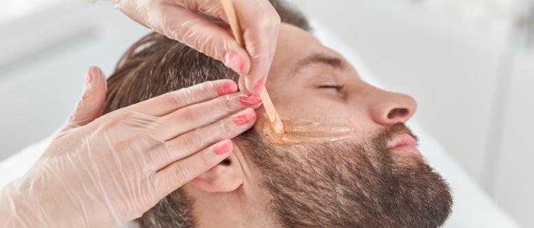 Concept of cosmetology and facial A woman beautician makes face and beard modeling for a man waxing epilation Depilation with wax Concept of cosmetology and facial A woman beautician makes face and beard modeling for a man waxing epilation Depilation with wax