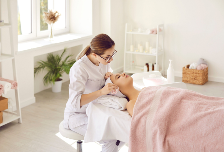 Beautician, cosmetologist or dermatologist cleaning skin on woman's face after chemical peel. Specialist at spa salon wiping young lady's face with wet towel after doing professional facial treatment