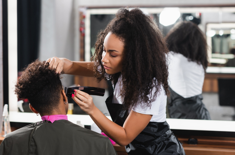 African american hairdresser in apron trimming head of client in salon