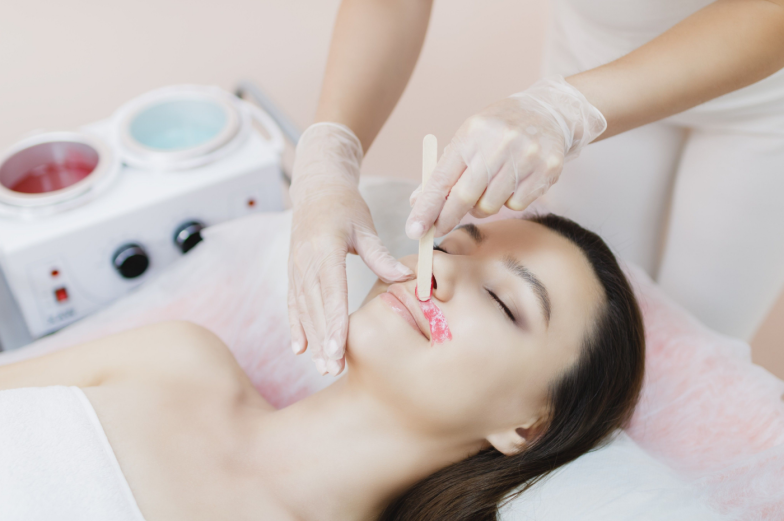 A master applies depilatory wax to the face of a beautiful young woman to remove unwanted hair. Sugaring. Depilation. Epilation. Beauty concept. Selective focus.