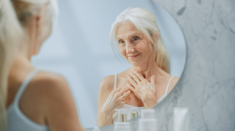 Beautiful Senior Woman Morning Bathroom Routine, Looks into Mirror Touches Her Neck with Sensual Movement of Hands