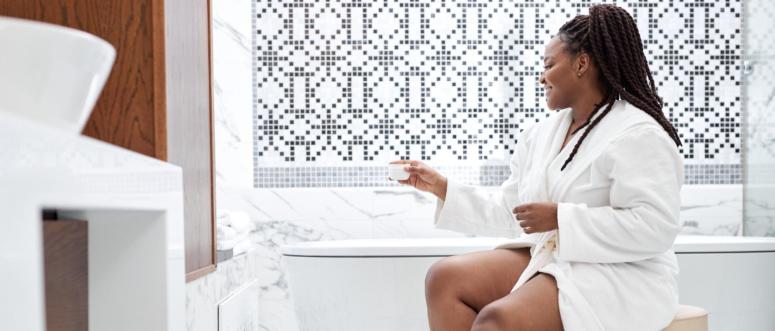 afro american woman in bathrobe spending morning in bathroom applying moisturizing cream on shaved and soft legs afro american woman in bathrobe spending morning in bathroom applying moisturizing cream on shaved and soft legs