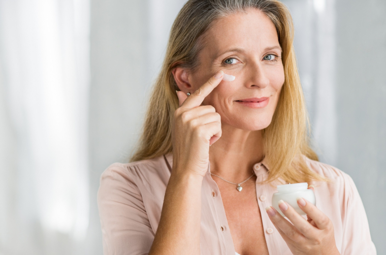 Smiling senior woman applying anti-aging lotion to remove dark circles under eyes. Happy mature woman using cosmetic cream to hide wrinkles below eyes. Lady using day moisturizer.