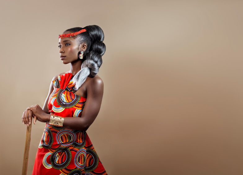 Beautiful confident African woman with intricate hair wearing an African print dress holding a wooden stick confidently