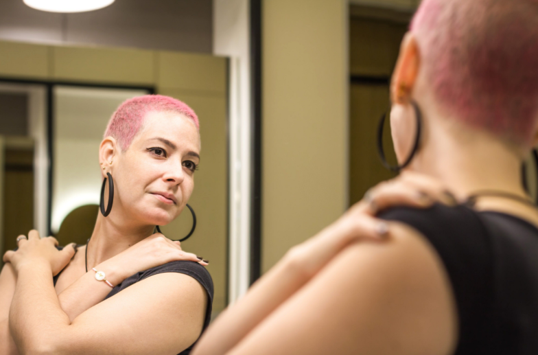 Healthy woman after chemotherapy looks in mirror at herself with love and hope. Girl with short hair. Self love and health. Body positive