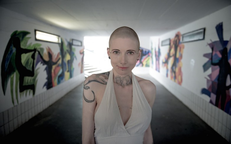 bald woman wearing white surplice sleeveless top taking self portrait inside tunnel with graffiti tagged wall