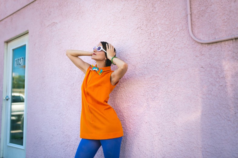 woman wearing orange sleeveless shirt and blue pants near pink painted wall during daytime photo