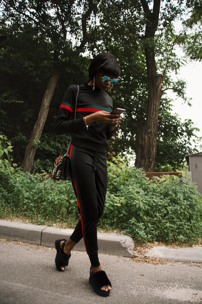 Woman in Black, Green, and Red Gucci Sweatshirt and Sweatpants Using Smartphone