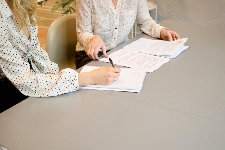 woman signing on white printer paper beside woman about to touch the documents photo